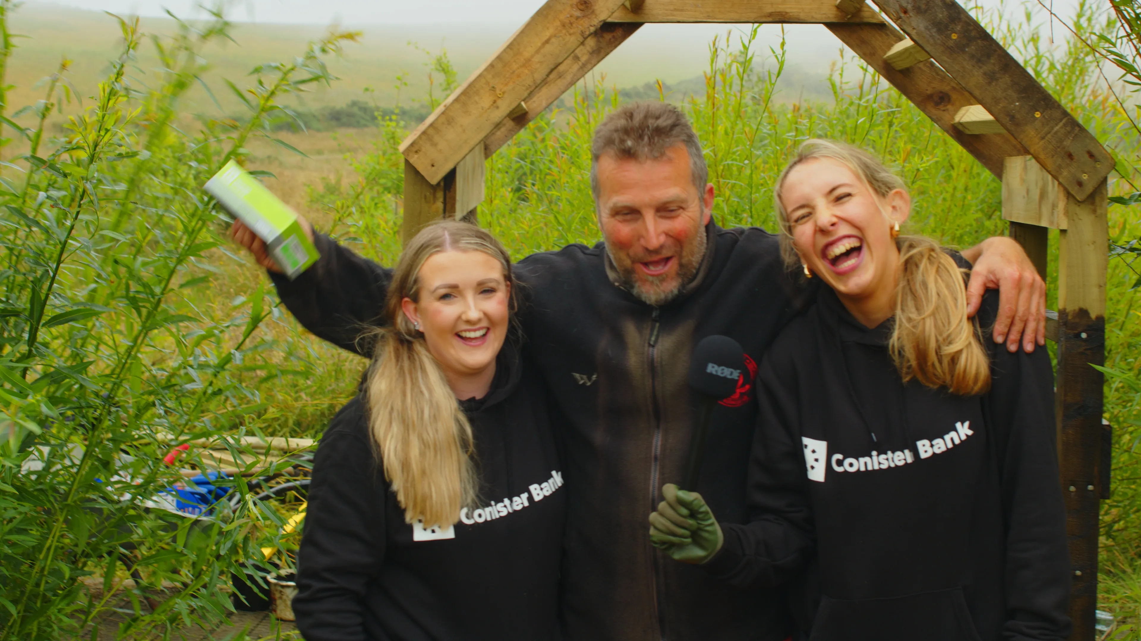 Three Conister Bank staff members celebrating at the completed garden structure during the volunteer week at The Children's Centre, Isle of Man, filmed by DotPerformance
